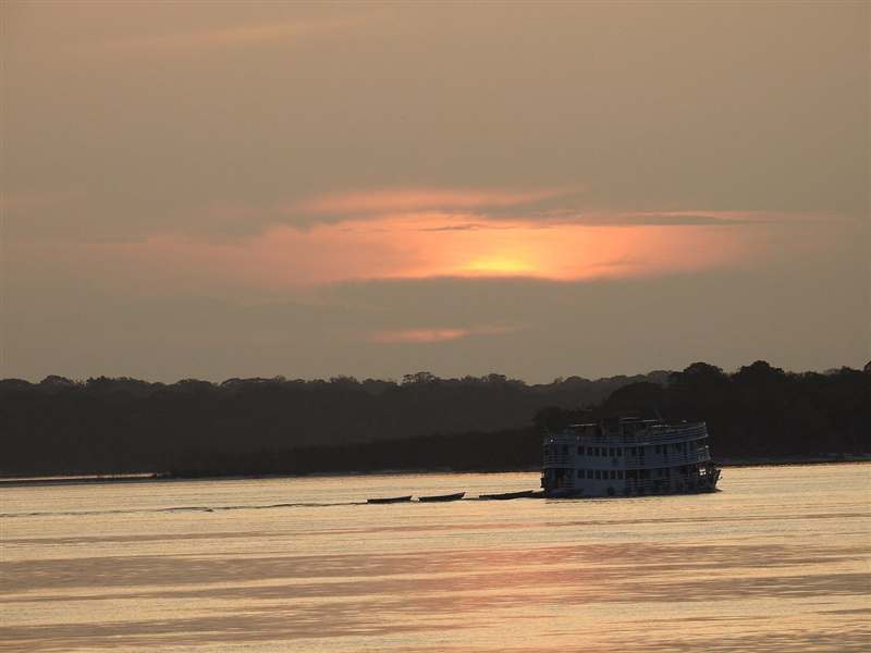 Barco-hotel de pesca esportiva navegando em rio amazônico ao pôr do sol